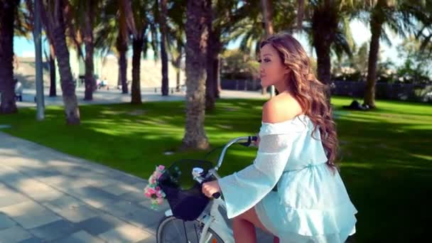 Mavi elbiseli Asyalı model yeşil bir parkta beyaz bir bisiklet sürmek — Stok video