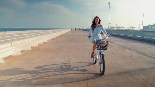 Modelo asiático en un vestido azul monta una bicicleta blanca en la terraza del mar — Vídeo de stock