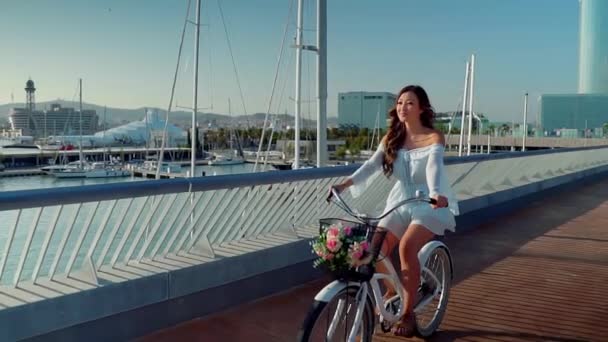 Aziatische model in een blauwe jurk rijdt op een witte fiets op zee terras — Stockvideo