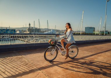 Mavi elbiseli Asyalı model yeşil bir parkta beyaz bir bisiklet sürmek