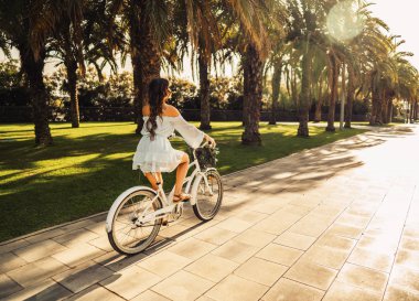 Mavi elbiseli Asyalı model yeşil bir parkta beyaz bir bisiklet sürmek