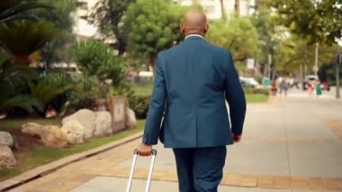 Seyahat çantası veya bavulile yürürken mavi takım elbise giyen Hintli işadamı