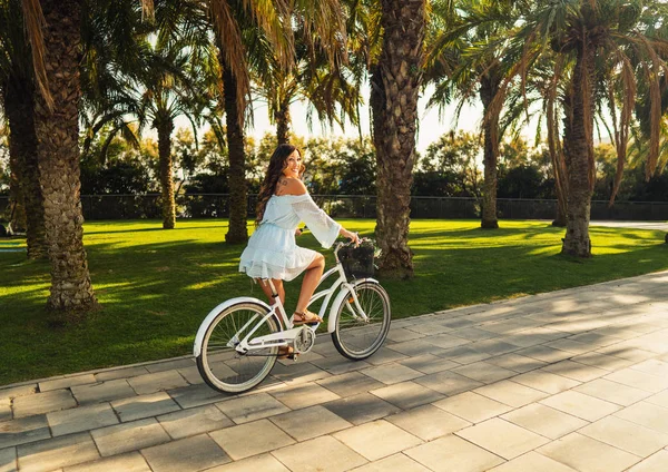 Asian model in a blue dress rides a white bicycle in a green park