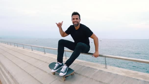 Skateboarder se sienta con monopatín en la moderna terraza del mar de la ciudad — Vídeos de Stock