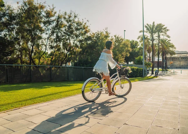 Азиатская модель в синем платье катается на белом велосипеде в зеленом парке — стоковое фото