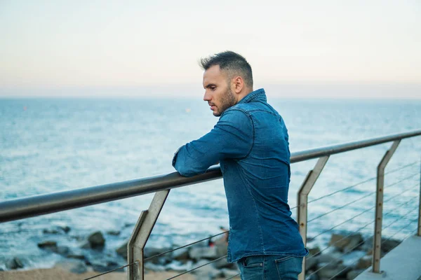 Um jovem e bonito homem na ponte perto da bela praia . — Fotografia de Stock