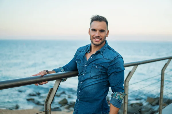 Um jovem e bonito homem na ponte perto da bela praia . — Fotografia de Stock