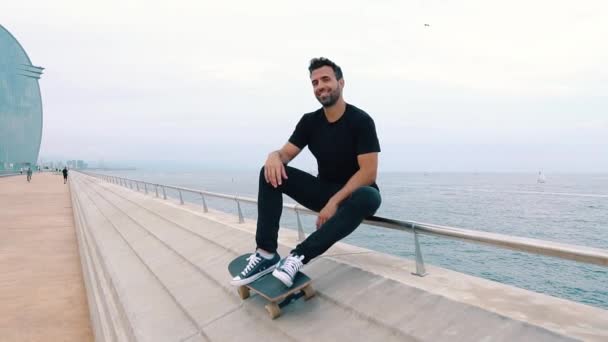 Skateboarder sitting with skateboard in the modern city street promenade — Stock Video