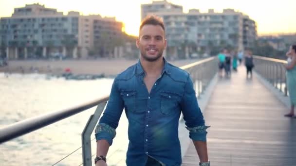 Ein junger gutaussehender Mann auf der Brücke in der Nähe des schönen Strandes. — Stockvideo