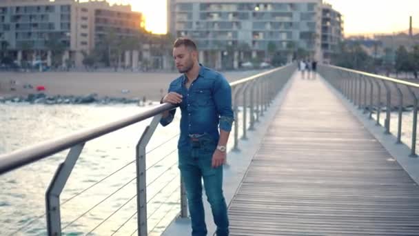 Ein junger gutaussehender Mann auf der Brücke in der Nähe des schönen Strandes. — Stockvideo
