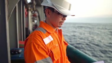 Filipinli güverte subayı kıyı gemisinin güvertesinde kontrol listesini dolduruyor. Denizdeki evrak işleri.