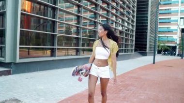 Güzel atletik kız modern şehirde uzun bir sörf tahtası kullanıyor.