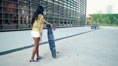 Güzel atletik kız modern şehirde uzun bir sörf tahtası kullanıyor.