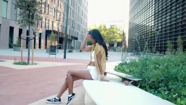 在现代城市里，一个漂亮的运动姑娘坐在长板上 — 图库视频影像