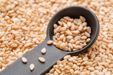 Siyah kaşıkta susam tohumlarının üzerine beyaz susam tohumu..