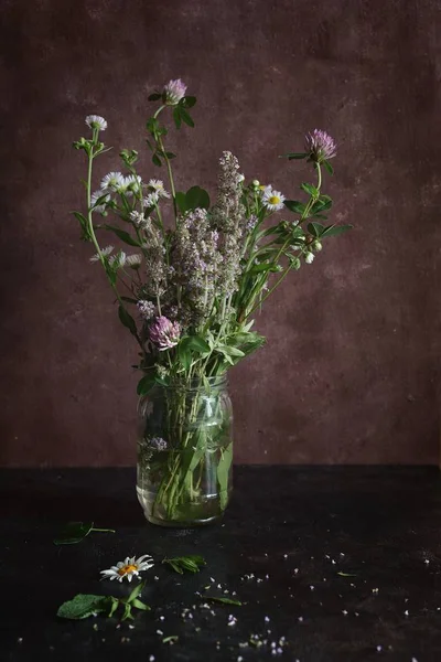 karanlık bir arka plan üzerinde bir cam kavanoza otlar ve kır çiçekleri buketi. Pembe çiçek yonca