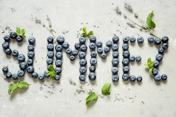 The inscription is laid out of berries and lavender flowers on a gray background. Flat lay, top view. Summer