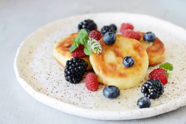  Pazar kahvaltısı peynirli kek, bal, taze meyveler ve nane ile. Krep peynir veya lor börek bal ve çilek plaka mavi masa üstü görünümünde dekore edilmiştir. Sağlıklı ve diyet kahvaltı.