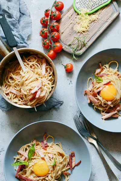 Pasta carbonara with bacon and parmesan in gray plates on the table, restaurant serve. Traditional Italian cuisine. Home family dinner.View from above