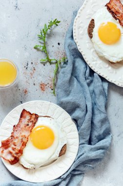Tabak kızarmış yumurta, pastırma ve gri arka plan üzerinde çavdar ekmeği tost ile kahvaltı. İngiliz kahvaltısı, portakal suyu