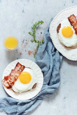 Tabak kızarmış yumurta, pastırma ve gri arka plan üzerinde çavdar ekmeği tost ile kahvaltı. İngiliz kahvaltısı, portakal suyu