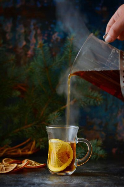 Christmas tea with orange and spices. Selective focus. Hot spicy tea on tray with branches of coniferous tree. Christmas concept on dark wooden background