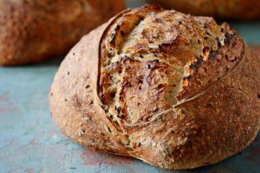 Gri-mavi arka plan, taze ev yapımı ekmek kepekli un üzerinde keten tohumu ile. Fransız ekmeği yuvarlak şekli. Ekmek pişirme. Mayasız ekmek