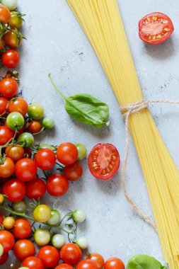 Gıda çerçeve. Makarna malzemeler kavramı. Pişmemiş makarna ve kiraz domates ile mavi bir arka plan üzerinde yeşil fesleğen. Üstten görünüm kopya alanı ile. Italyan Mutfagi