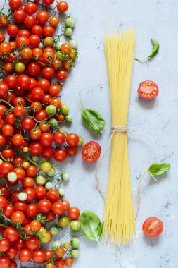 Gıda çerçeve. Makarna malzemeler kavramı. Pişmemiş makarna ve kiraz domates ile mavi bir arka plan üzerinde yeşil fesleğen. Üstten görünüm kopya alanı ile. Italyan Mutfagi