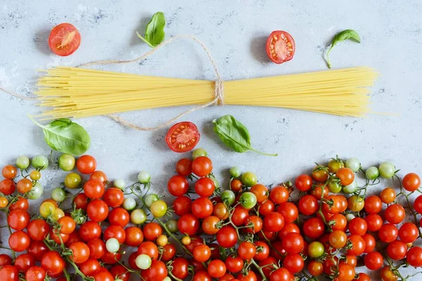 Food frame. Pasta ingredients concept. Uncooked spaghetti and cherry tomato with green basil on a blue background. Top view with copy space. Italian food