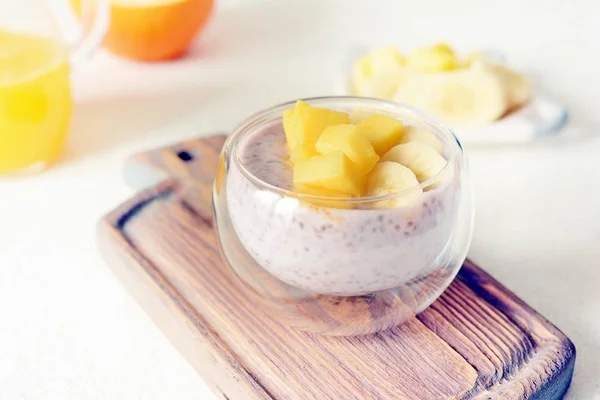 Chia pudding with mango pulp  in beautiful glasses with green mint leaves and cut fresh ripe tropical fruit, orange juice for breakfast on a light background - raw vegetarian sweet organic dessert.