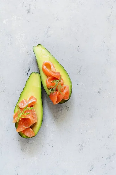 Ripe avocado boats with slices of salted trout, salmon and fresh greens on a gray background. Avocado boats stuffed with salmon with lime, spinach leaves and arugula, concept healthy food, diet.