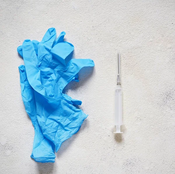 Blue medical gloves and a medical syringe on a light textured background. Vaccination items, shots, Copy space