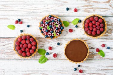 Çikolata ganache 'li ahududu ve yaban mersinli tartlar, taze böğürtlen ve nane yaprağı, seçici odaklanma. Beyaz arka planda taze meyveli tart, masada taze ev yapımı meyveli kek.