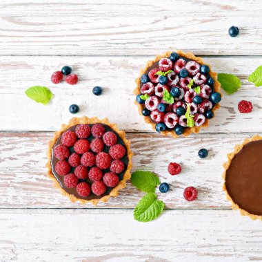 Çikolata ganache 'li ahududu ve yaban mersinli tartlar, taze böğürtlen ve nane yaprağı, seçici odaklanma. Beyaz arka planda taze meyveli tart, masada taze ev yapımı meyveli kek.