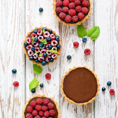 Çikolata ganache 'li ahududu ve yaban mersinli tartlar, taze böğürtlen ve nane yaprağı, seçici odaklanma. Beyaz arka planda taze meyveli tart, masada taze ev yapımı meyveli kek.
