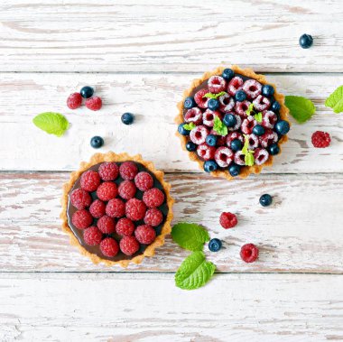 Çikolata ganache 'li ahududu ve yaban mersinli tartlar, taze böğürtlen ve nane yaprağı, seçici odaklanma. Beyaz arka planda taze meyveli tart, masada taze ev yapımı meyveli kek.