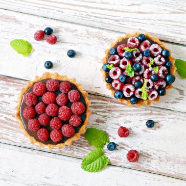 Çikolata ganache 'li ahududu ve yaban mersinli tartlar, taze böğürtlen ve nane yaprağı, seçici odaklanma. Beyaz arka planda taze meyveli tart, masada taze ev yapımı meyveli kek.
