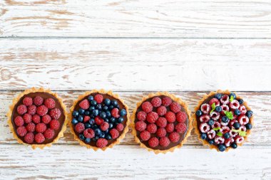Çikolata ganache 'li ahududu ve yaban mersinli tartlar, taze böğürtlen ve nane yaprağı, seçici odaklanma. Beyaz arka planda taze meyveli tart, masada taze ev yapımı meyveli kek.