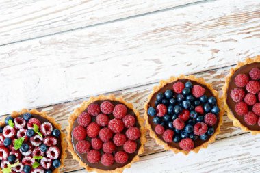 Çikolata ganache 'li ahududu ve yaban mersinli tartlar, taze böğürtlen ve nane yaprağı, seçici odaklanma. Beyaz arka planda taze meyveli tart, masada taze ev yapımı meyveli kek.