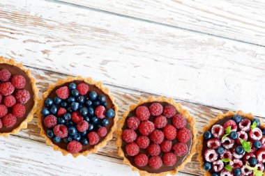 Çikolata ganache 'li ahududu ve yaban mersinli tartlar, taze böğürtlen ve nane yaprağı, seçici odaklanma. Beyaz arka planda taze meyveli tart, masada taze ev yapımı meyveli kek.