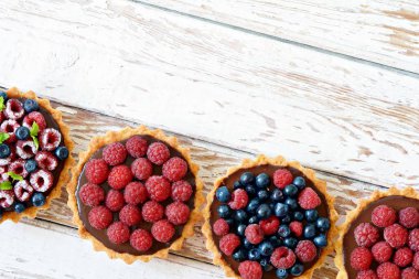 Çikolata ganache 'li ahududu ve yaban mersinli tartlar, taze böğürtlen ve nane yaprağı, seçici odaklanma. Beyaz arka planda taze meyveli tart, masada taze ev yapımı meyveli kek.