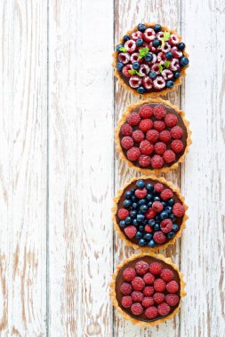 Çikolata ganache 'li ahududu ve yaban mersinli tartlar, taze böğürtlen ve nane yaprağı, seçici odaklanma. Beyaz arka planda taze meyveli tart, masada taze ev yapımı meyveli kek.