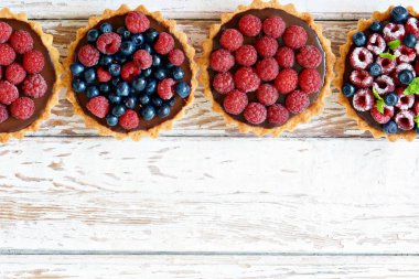 Çikolata ganache 'li ahududu ve yaban mersinli tartlar, taze böğürtlen ve nane yaprağı, seçici odaklanma. Beyaz arka planda taze meyveli tart, masada taze ev yapımı meyveli kek.