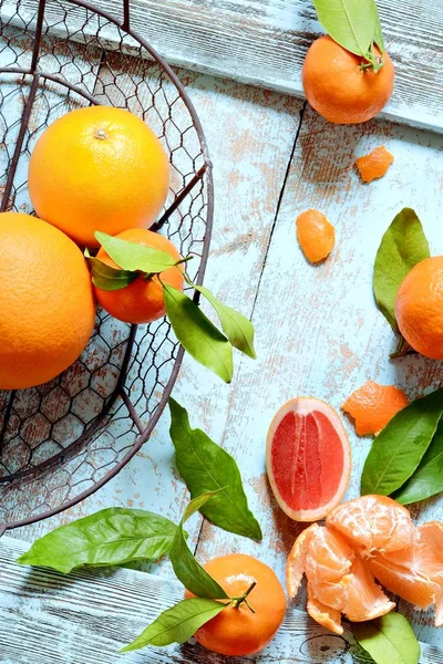 Tangerines (oranges, mandarins, clementines, citrus fruits) with leaves in basket on a mint (blue) background. Mandarin oranges with leaves in white basket on rustic wood background. Citrus