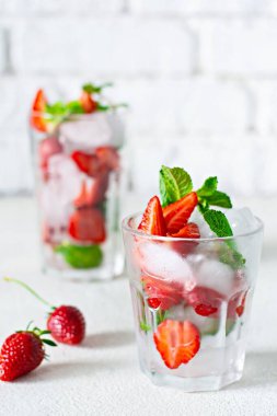 Buzlu su, çilek şurubu, taze çilek ve beyaz arka planda cam bir fincanda nane şekeri. Ferahlatıcı bir çilek içeceği..