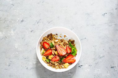 Beyaz bir tabakta fındıklı, kurutulmuş meyveli gevrek, taze çilek, nane ve yoğurt (mayalanmış süt). Sağlıklı kahvaltı kavramı.