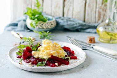 Cevizli pancar, aromatik otlar ve roka karışımıyla çırpılmış yumurta. Lezzetli sağlıklı kahvaltı. Beyaz tabakta soslu pancar carpaccio..