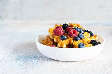 Kahvaltıda hafif arka planda beyaz bir kasede böğürtlenli waffle..