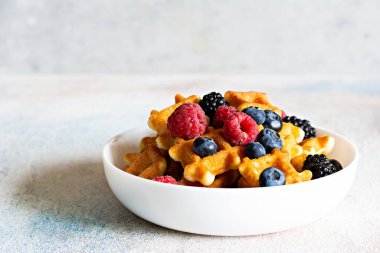 Kahvaltıda hafif arka planda beyaz bir kasede böğürtlenli waffle..